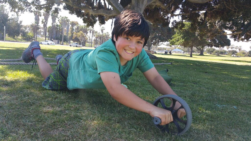 Youth athlete performing ab wheel exercise during outdoor fitness program at San Diego park